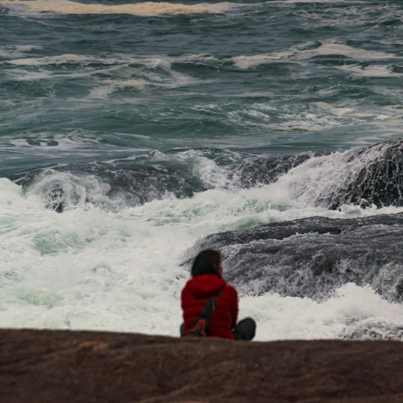 A person standing calmly on a rock overlooking a stormy sea, symbolizing resilience and inner strength amidst life's challenges