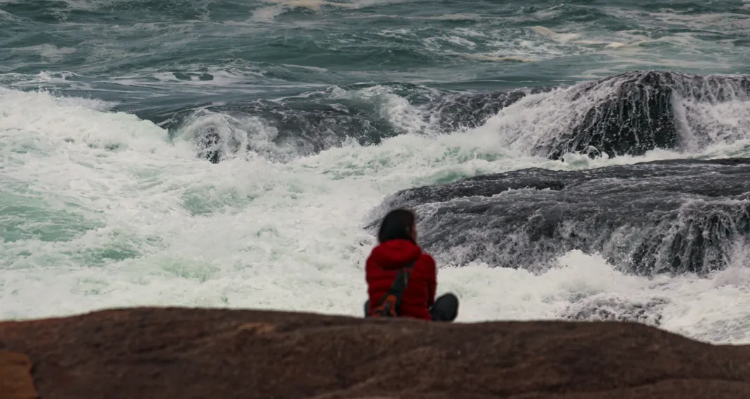 A person standing calmly on a rock overlooking a stormy sea, symbolizing resilience and inner strength amidst life's challenges