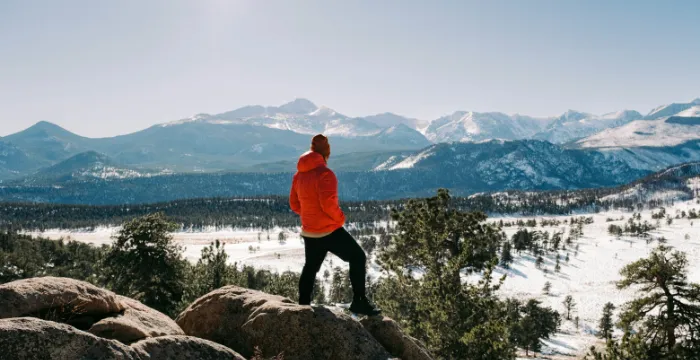 A person standing on a mountain peak, maintaining perspective and optimism while contemplating the future and overcoming adversity