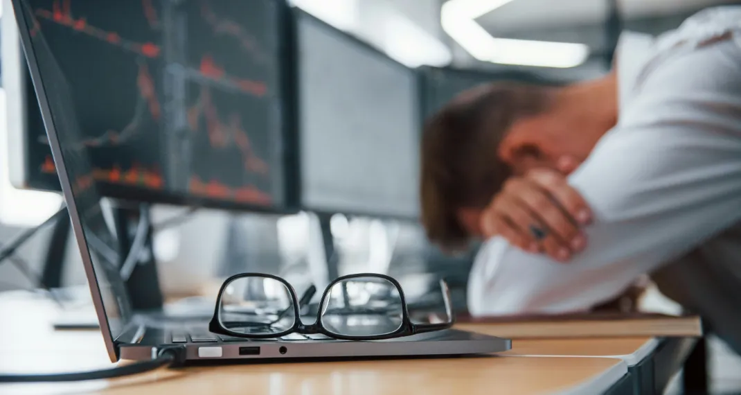 A visibly tired person resting their head on a desk next to a laptop, symbolizing the overwhelming feeling of burnout and mental fatigue
