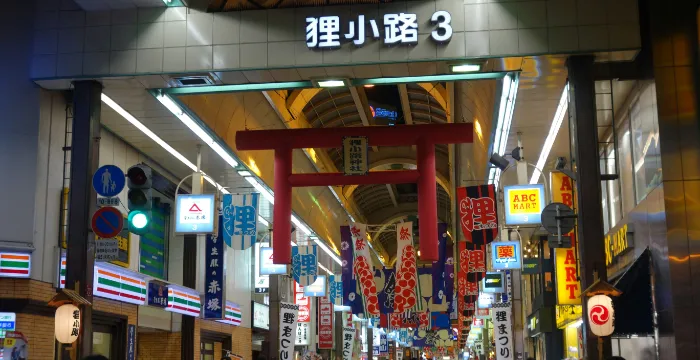 A bustling, narrow, covered street of Nishiki Market in Kyoto, Japan, lined with stalls selling various Japanese street foods, snacks and local delicacies.