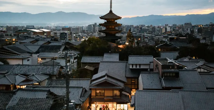 The iconic wooden stage of Kiyomizu-dera Temple in Higashiyama, Kyoto, overlooking a sea of cherry blossoms with the city skyline in the background.