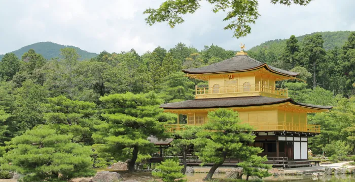 The magnificent Golden Pavilion (Kinkaku-ji) in Kyoto, its top two floors covered in gold leaf, perfectly reflected in the tranquil waters of the surrounding Mirror Pond, set within a classic Japanese strolling garden.