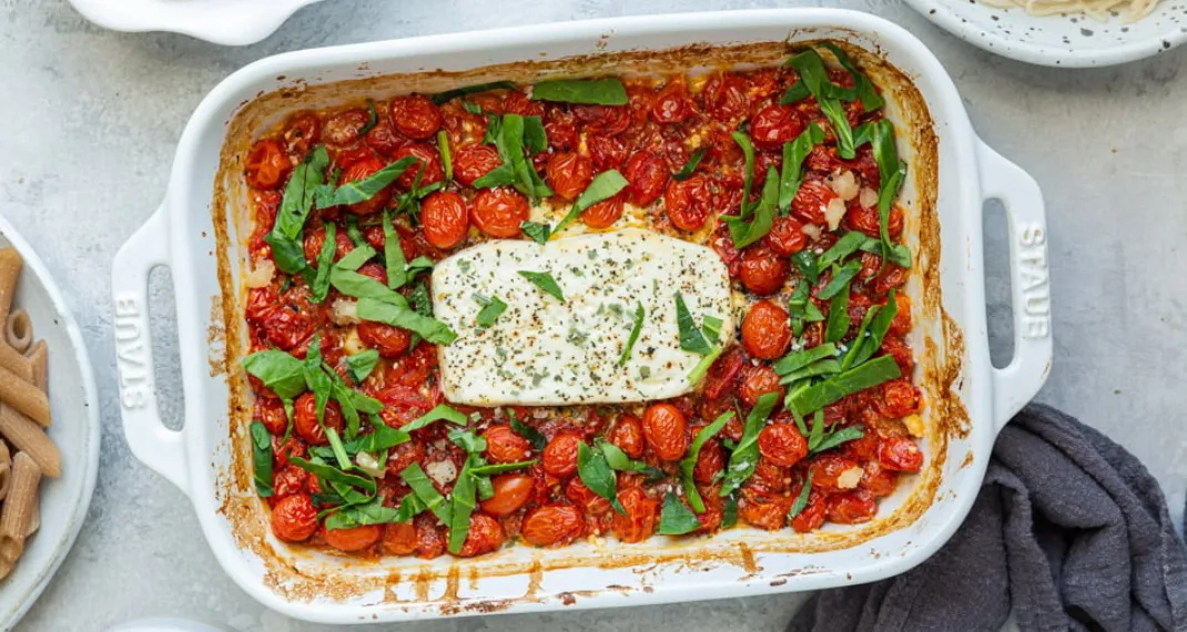 Large baking dish with molten, creamy feta cheese, burst cherry tomatoes and fresh basil mixed with cooked pasta